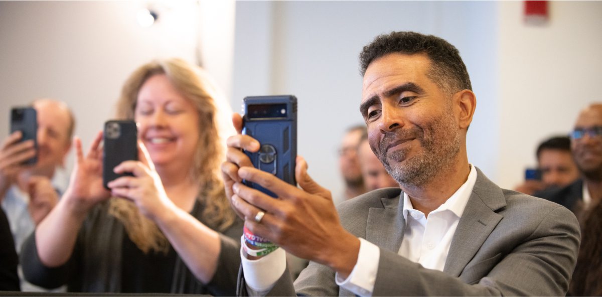 Man holding up cellphone while smiling at meeting